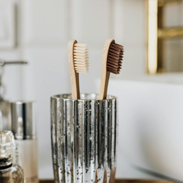 Eco friendly bamboo toothbrushes in silver glass placed in bathroom near sink and beauty products